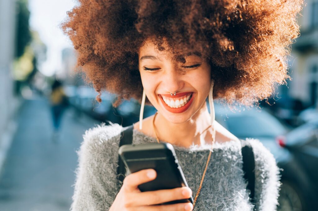 Joyful woman laughing at her phone on a sunny city street